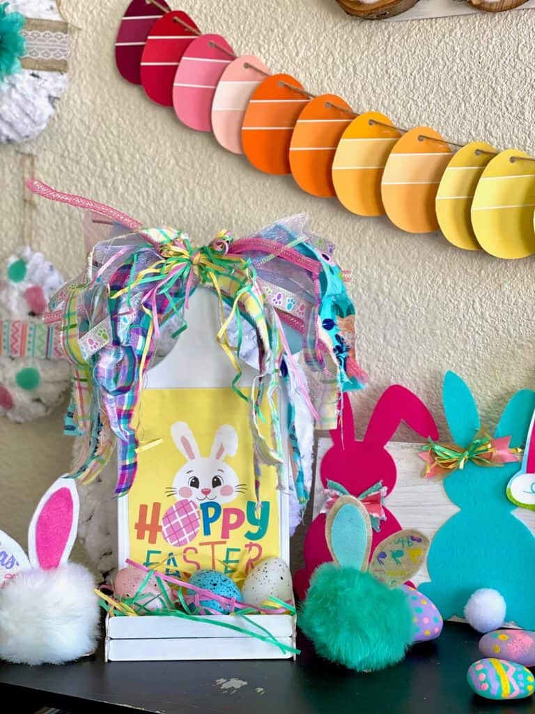 DIY Cutting board craft project with a Hoppy Easter bunny gift bag and a huge scrappy fabric bow with some other Easter decor staged around it.