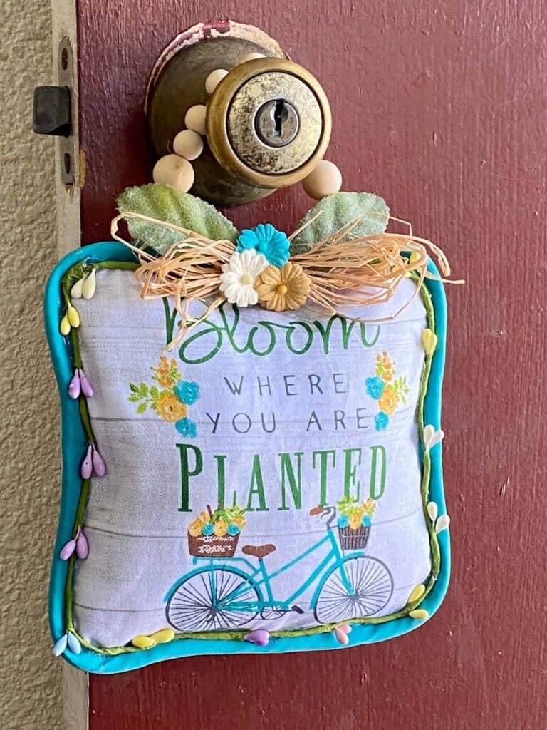 Dollar Tree 'Bloom Where you Are Planted' Pot Holder DIY Doorknob Hanger with a raffia bow and wood bead hanger.