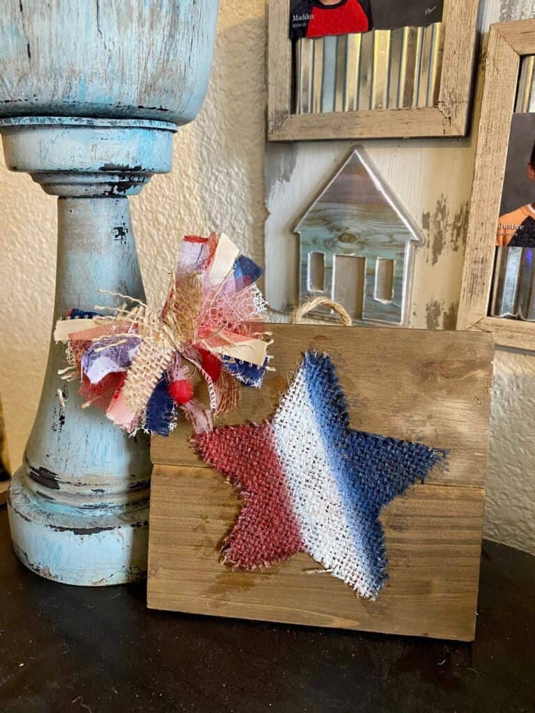 Easy Patriotic Red, white, and blue burlap star with a messy bow for July 4th next to a chunky distressed candlestick.