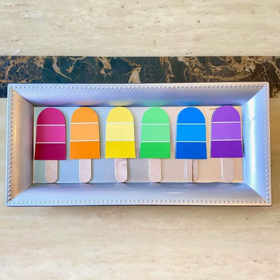 6 Paint sample popsicles, one of each color of the rainbow on a dollar tree charger plate that's silver before it was painted.