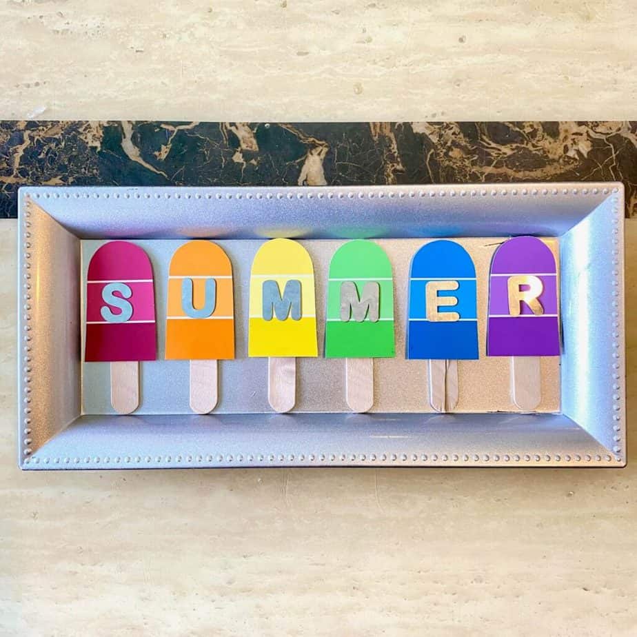 6 Paint swatch popsicles, one of each color of the rainbow on a dollar tree charger plate that's silver before it was painted, with galvanized letters that spell SUMMER, one letter on each popsicle.
