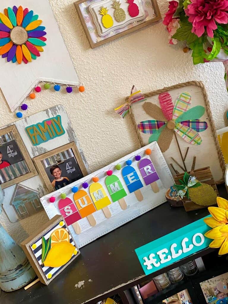 DIY Summer paint chip popsicles on a bookshelf with other summer crafts and decor next to a lemon shelf sitter and scrap fabric colorful flower.