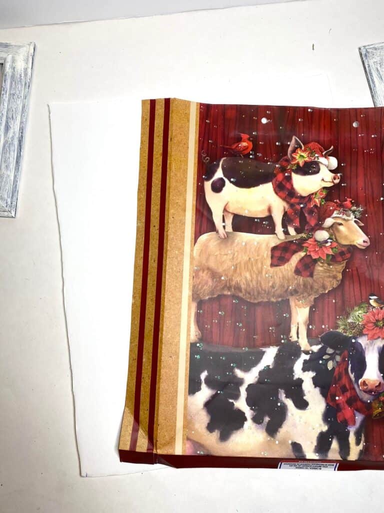 Front of a Dollar Tree Farmhouse Christmas Gift Bag with a cow, pig, and sheep standing on each others back, glued to a white foam board.