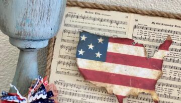 Dollar Tree DIY Fourth of July USA Freedom Flag Decor made with an America cutout and American flag paper on a music sheet background with nautical rope around the edge to celebrate the Americana Holiday.