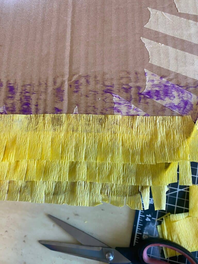 Strips of yellow crepe paper with fringe cut along the edges, glued to the front bottom of the cardboard piñata.