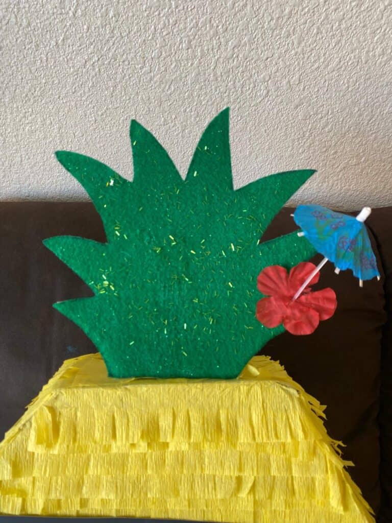 Green glitter pineapple crown on top of the Piñata with an Umbrella pic and a hibiscus flower.