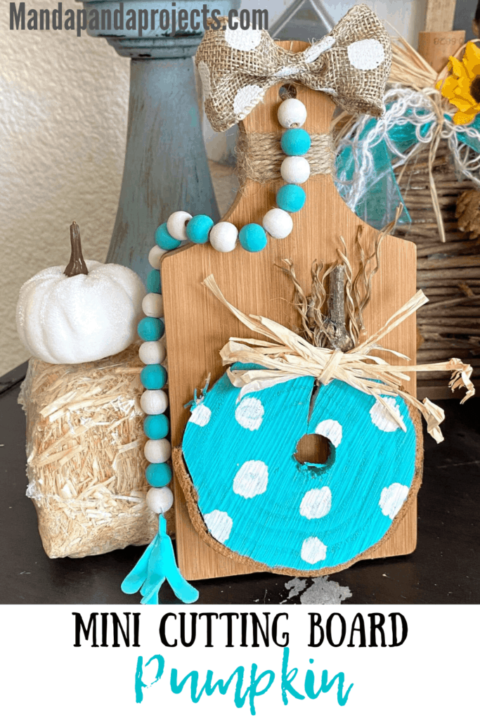 DIY Mini cutting board teal wooden pumpkin fall tiered tray decor with a wood bead garland next to a hay bale and a white pumpkin.