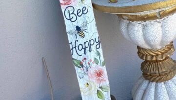 Upcycled Wooden Table Leg Porch Decor made with a 'Bee Happy' Dollar Tree transfer sticker and supplies with mustard colored polka dots sitting next to a gold and white distressed table.