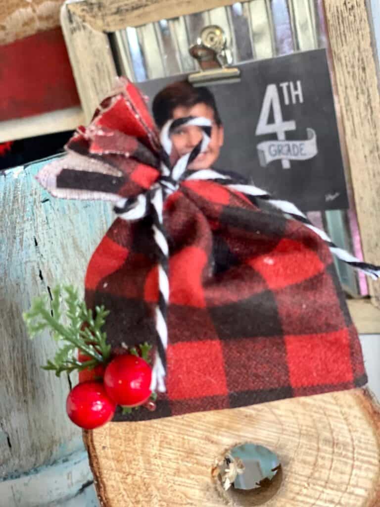 Red and black buffalo check winter hat with a Holly Berry sprig on top of the DIY wooden snowman craft.