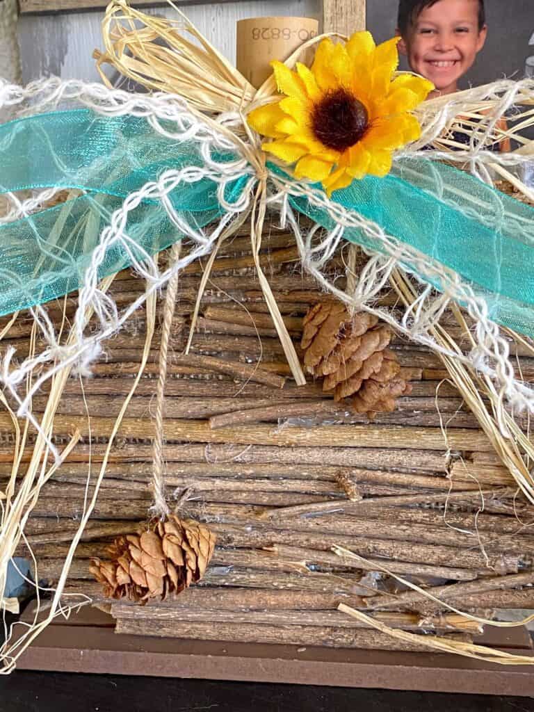Front of the dollar tree wooden stick pumpkin with the little pine cones dangling from a piece of twine.