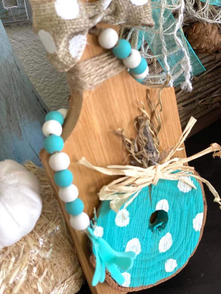 Birds eye view of the teal wooden pumpkin with white polka dots and a teal and white wood bead garland as decoration.