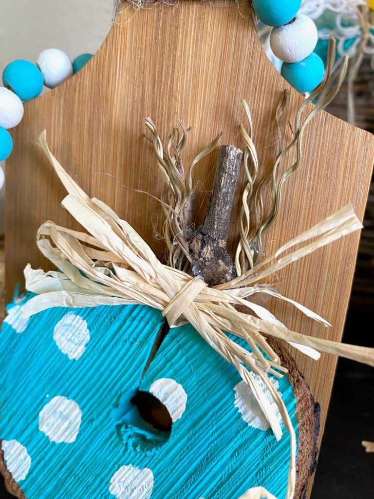 Close up of the wooden pumpkin stem made from a stick and a messy raffia bow,