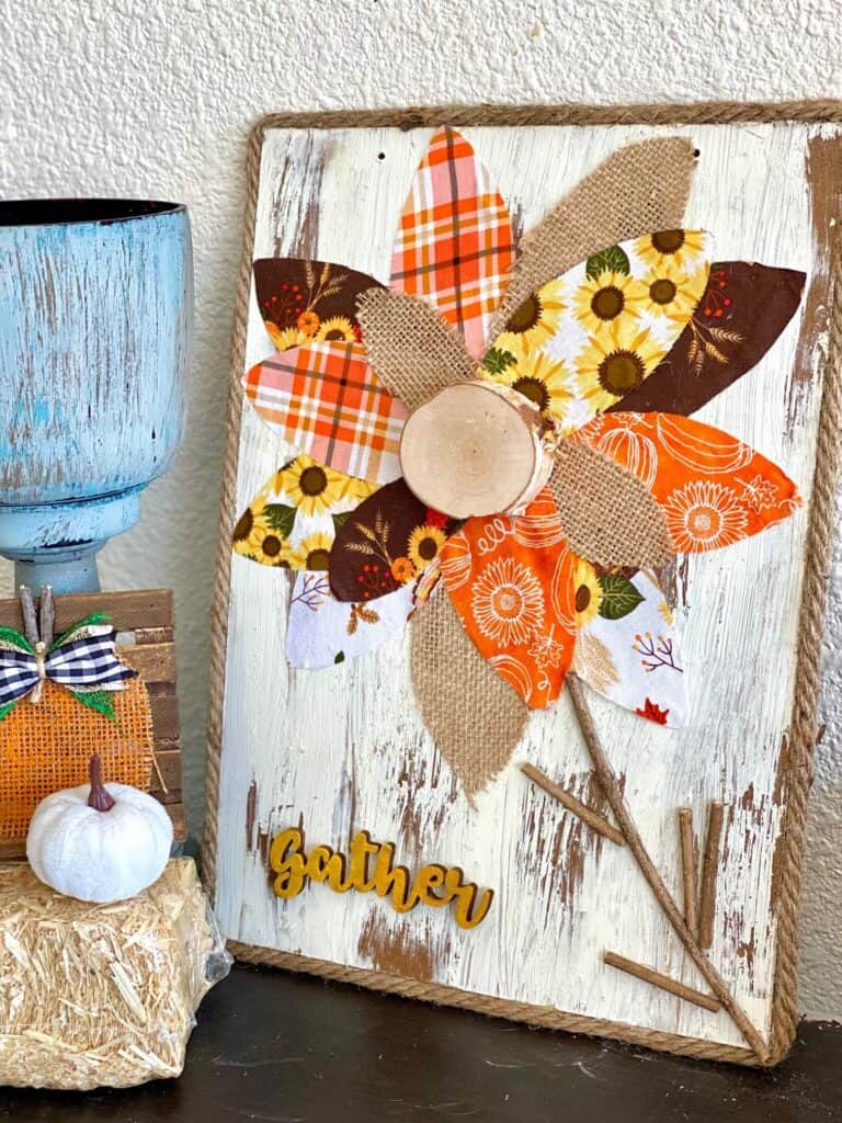 DIY Fall fabric and burlap sunflower with chippy paint background and jute rope rim and a wooden cutout of the word "gather". Autumn decor.