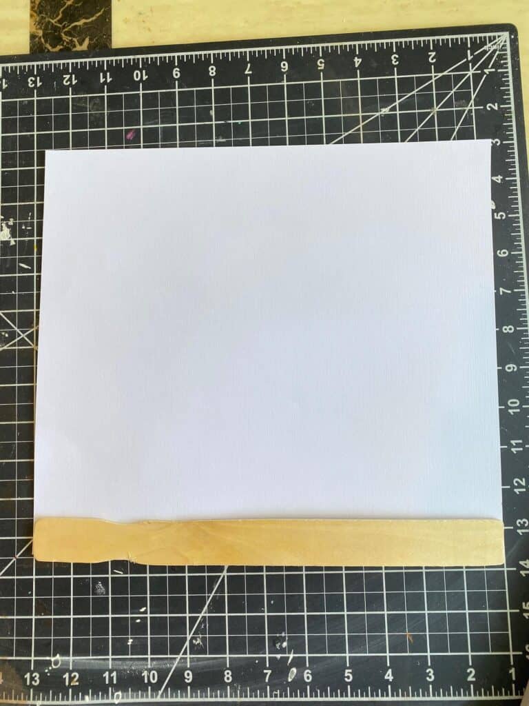 The back of a piece of scrapbpook paper with a paint stick being traced to cut out.