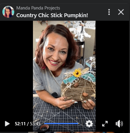 Amanda holding the completed wooden stick pumpkin on a facebook live.