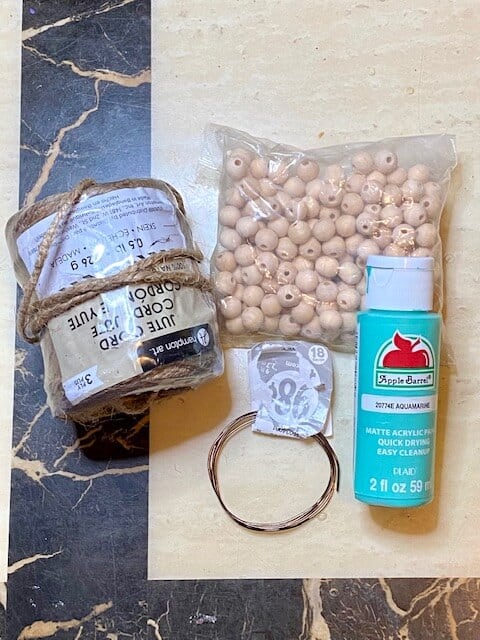 Supplies needed to make a wood bead pumpkin, twine, floral wire, teal paint, and wood beads.