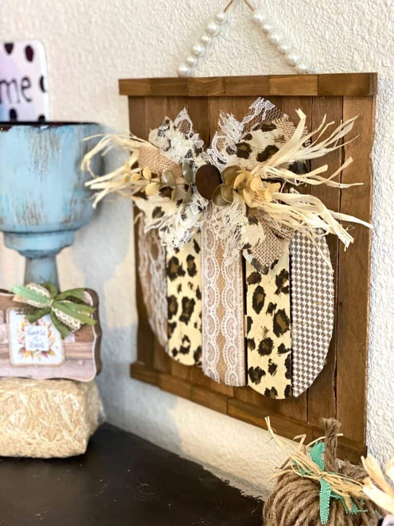 Dollar Tree leopard print pumpkin side view next to a mini hay bale with a little block decor and a chunky candlestick.