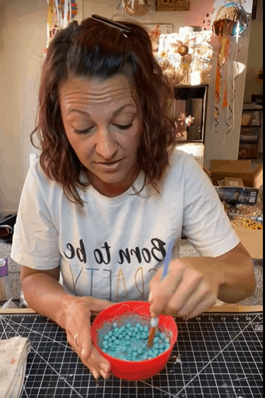 Amanda mixing the wooden beads with teal paint and water in a small bowl.