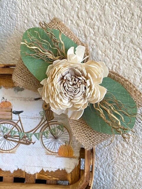 Simple and elegant burlap bow with lambs ear, a greenery sprig, and creme wood flower on the corner of the mini tobacco basket.