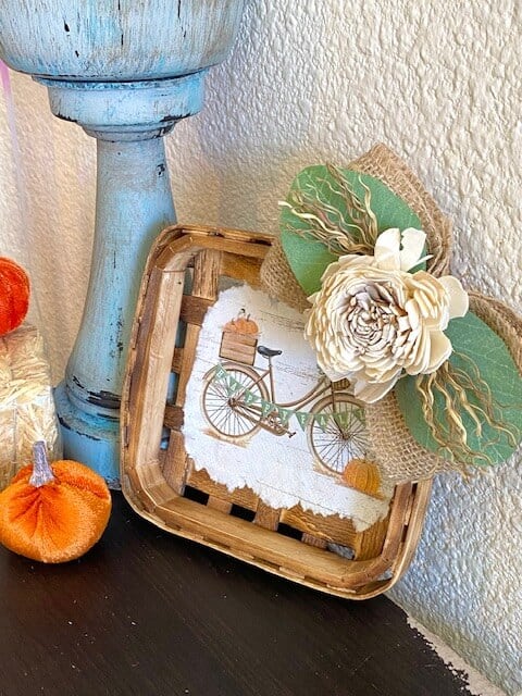 Fall Vintage Bicycle Tobacco Basket next to a candlestick on a bookcase with a velvet pumpkin.