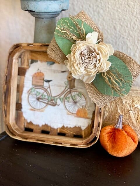 Fall Vintage Bicycle Tobacco Basket made with a cocktail napkin mod podged to the center of a small burlap bow with wood flower and lambs ear, next to a velvet pumpkin.