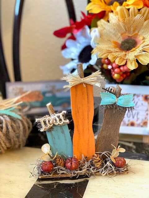 Paint stick pumpkin patch made with recycled ends of paint sticks for a DIY mini piece of fall decor for your tiered tray with Teal, orange and brown pumpkins and mini pinecones with spanish moss.