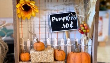 Dollar Tree mini pumpkin patch with hay bales, a white picket fence, and a sunflower and corn stalk.