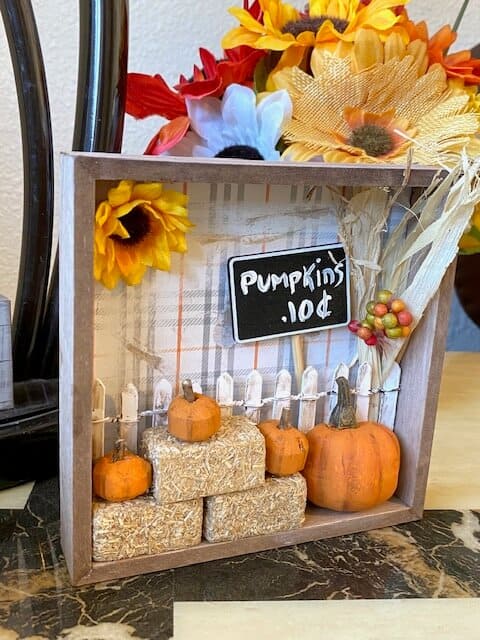 Dollar Tree mini pumpkin patch with hay bales, a white picket fence, and a sunflower and corn stalk.