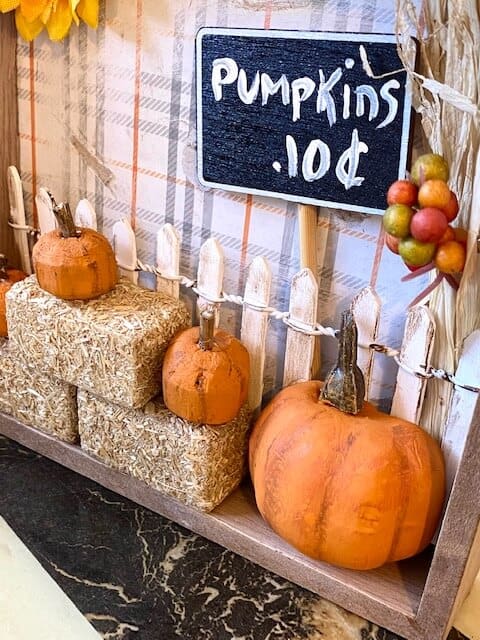 Close up of the mini pumpkins on the haybales with a white picket fence and a 10 cent pumpkins sign.