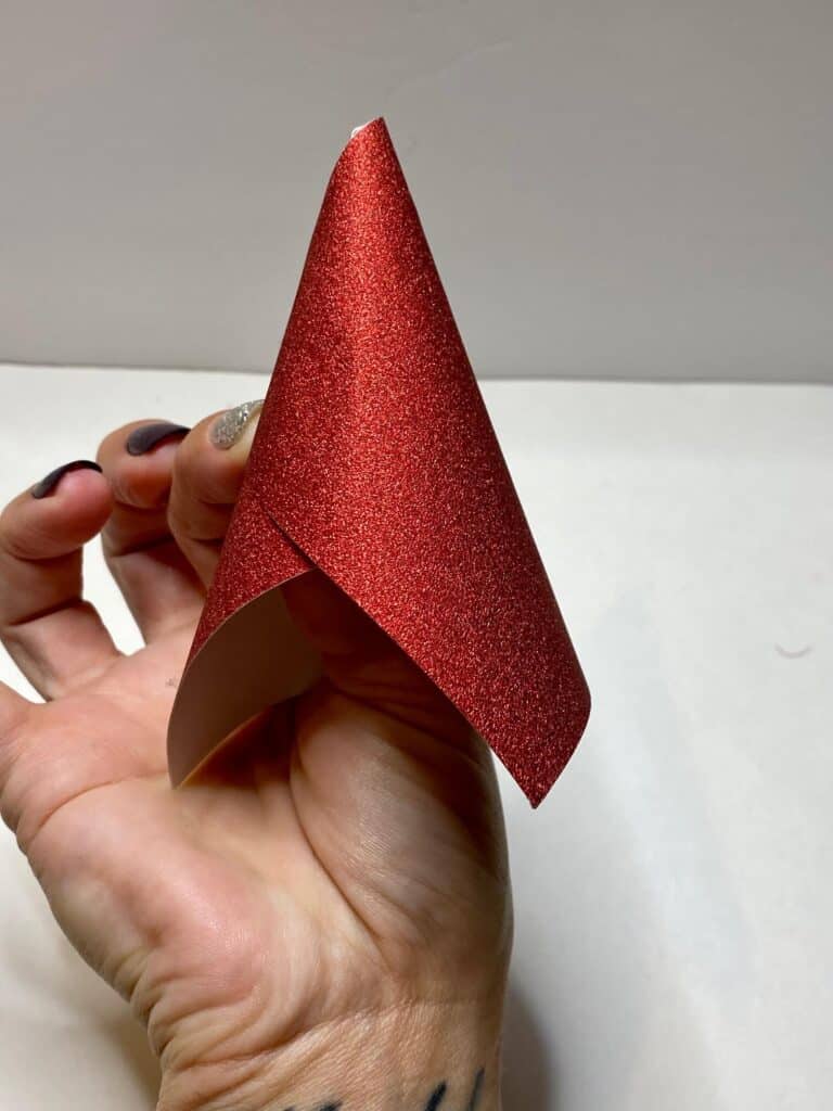 Fold a red glitter paper into a cone to make santa claus's hat.