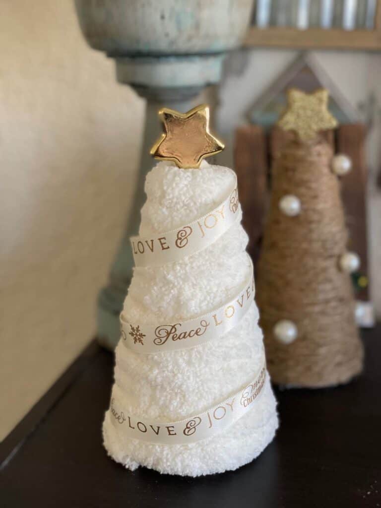 White chunky yarn wrapped foam cone with think white and gold  ribbon spiraled around it with a gold star on top.