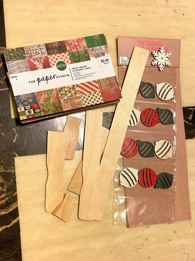 Supplies needed to make a paint stick Christmas tree with vintage pattern Christmas scrapbook paper by the paper studio and wooden ornament embellishments.
