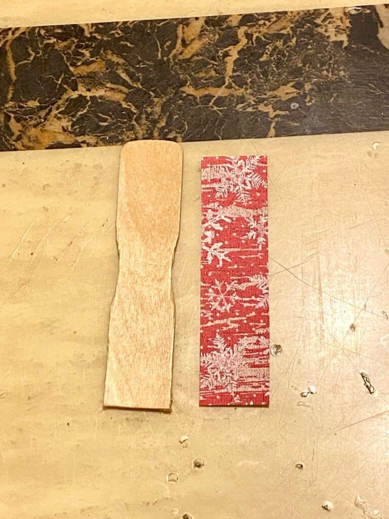 A small cut paint stick with a piece of red vintage Christmas scrapbook paper the same size.