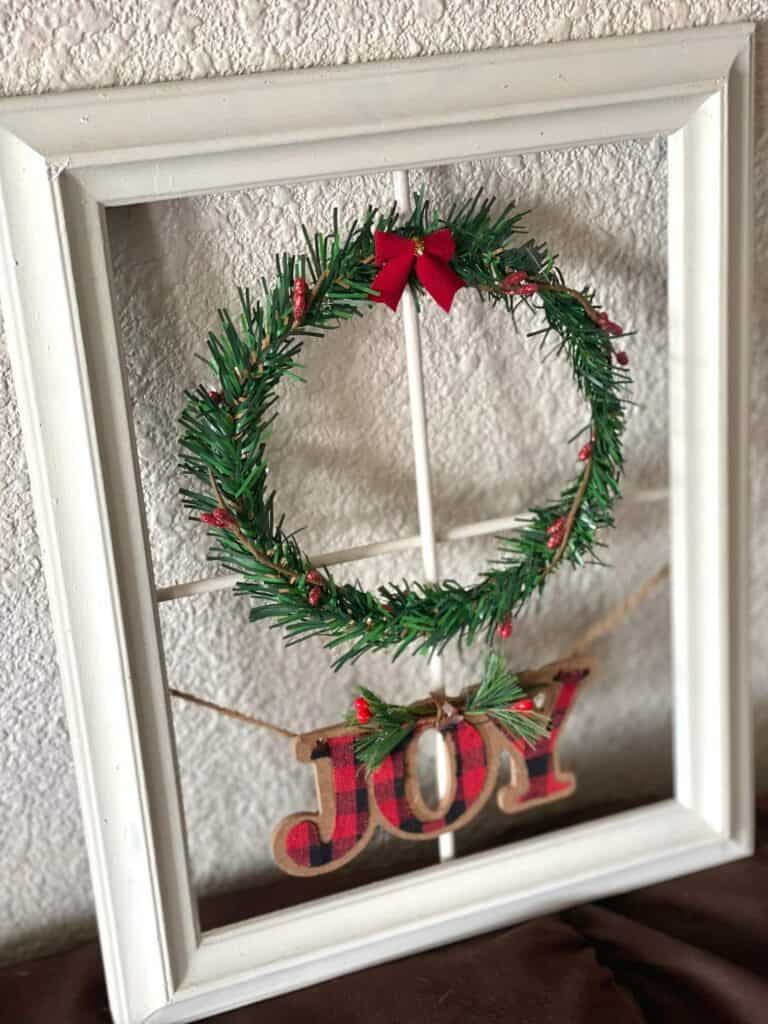 Close up of the Chrsitmas wreath with Joy ornament and the white frame window.