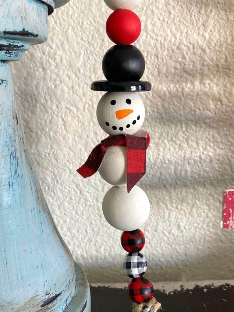 Snowman with a black top hat made out of wood beads with decorative buffalo check small beads on the end.