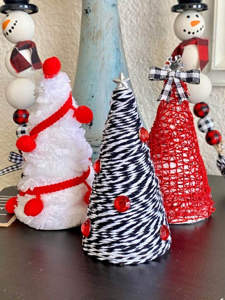 Mini Foam Cone Christmas Trees easy DIY Christmas decor for a red, black, and white theme decorations. 3 trees with white velvet yarn, red pom pom trim, and black and white bakers twine.