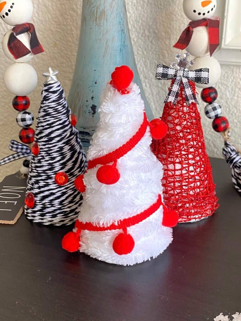 Mini Foam Cone Christmas Trees easy DIY Christmas decor for a red, black, and white theme decorations. 3 trees with white velvet yarn, red pom pom trim, and black and white bakers twine.