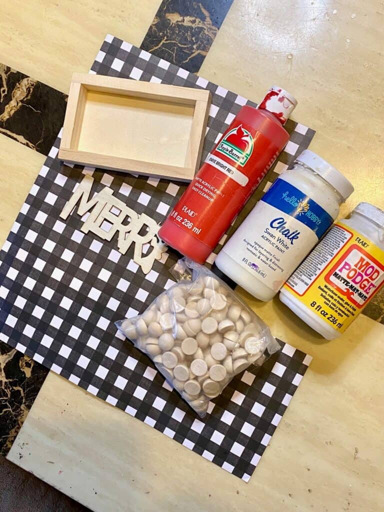 Supplies needed to make a Merry wooden tiered tray sitter with red, white, and black paint and buffalo check scrapbook paper with half wood beads.