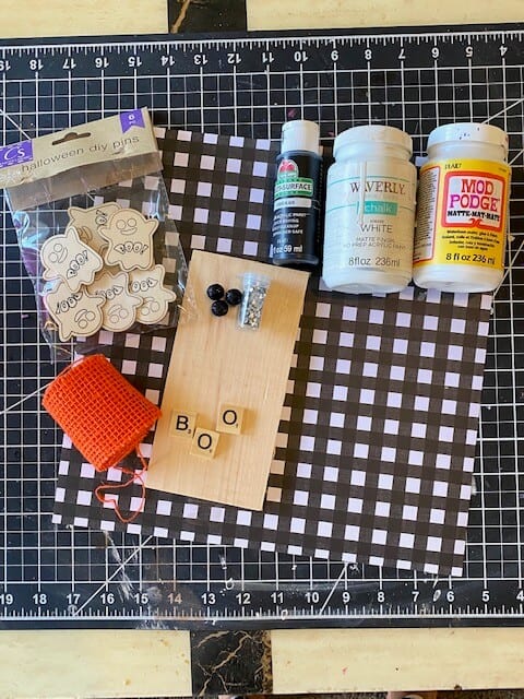 Supplies needed to make a DIY BOO Ghost decor for a tiered tray with buffalo check scrapbook paper, scrabble tiles, mini ghosts and orange burlap.