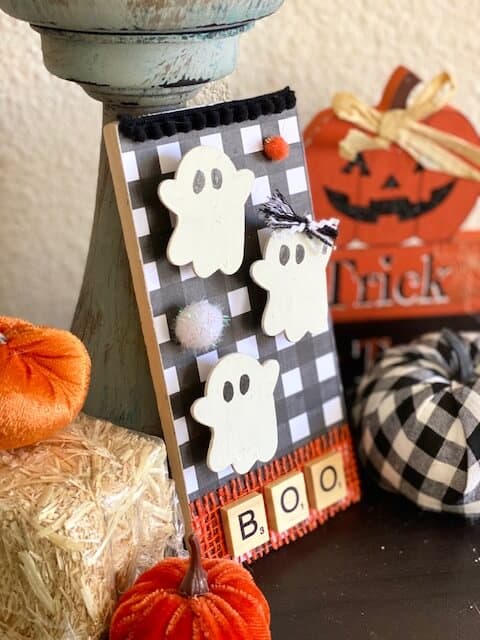 Dollar Tree DIY Ghost decor tiered tray sitter for a Halloween themed set up with BOO in scrabble tiles and a buffalo check background.