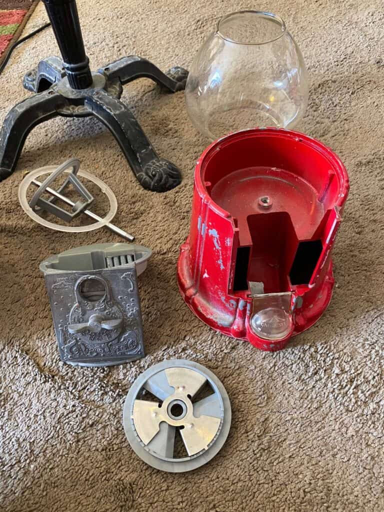 All of the different pieces of the vintage gumball machine taken apart and sitting on the floor.