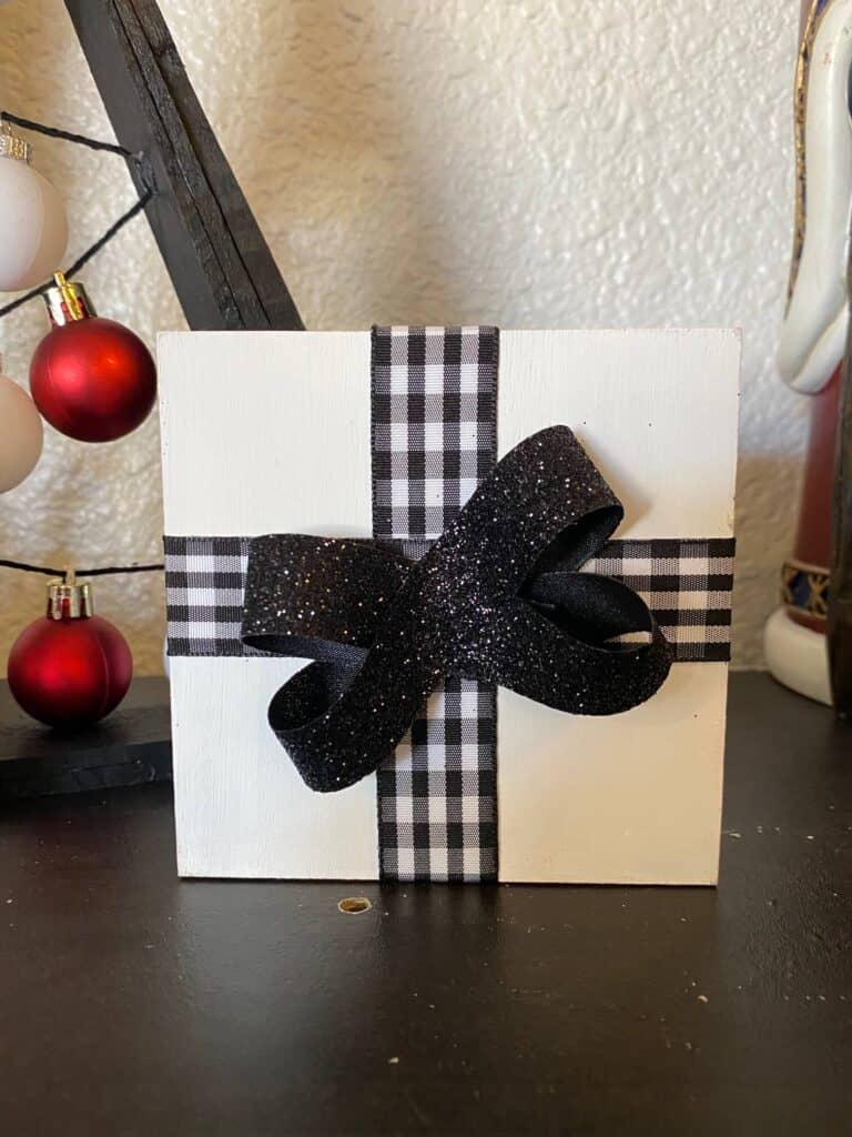 White wood block christmas present with black and white buffalo check ribbon and a black sparkly bow.