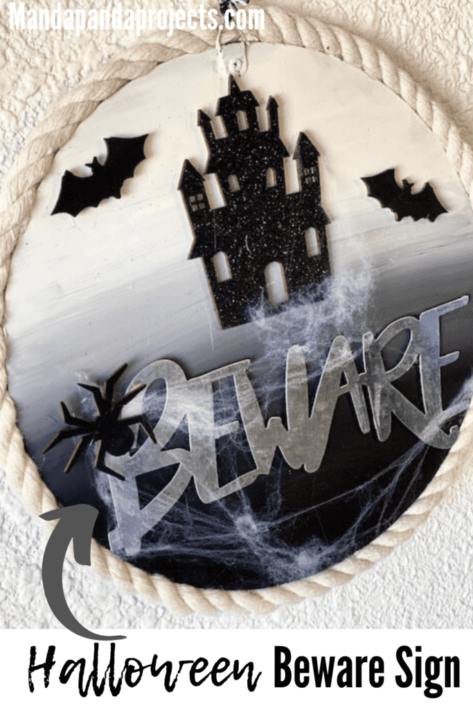 Dollar Tree DIY Halloween Beware sign for your front door with a haunted house, bats, and fake cobwebs, and nautical rope around the edge of the round wood sign.