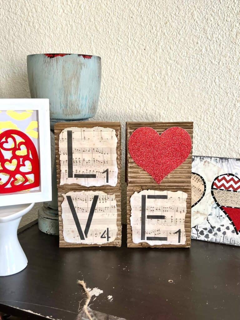 Love blocks with a red glitter heart for the "O" and corrugated cardboard with music sheet scrapbook paper with burnt edges on top, letters are stacked on top of each other.