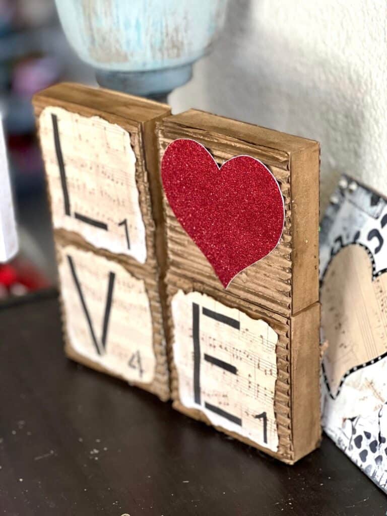 Love blocks with a red glitter heart for the "O" and corrugated cardboard with music sheet scrapbook paper with burnt edges on top.