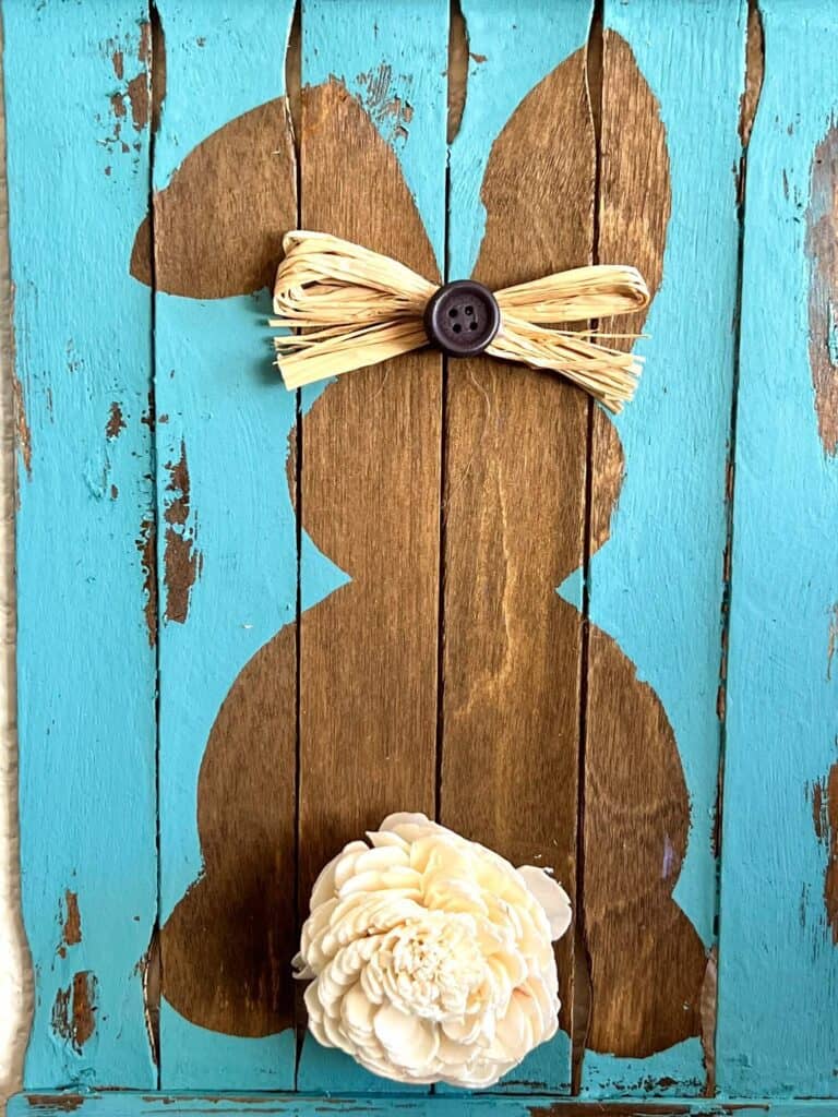 Close up of the wood reverse stenciled easter bunny with a raffia button bow in its ear and a sola wood flower tail.