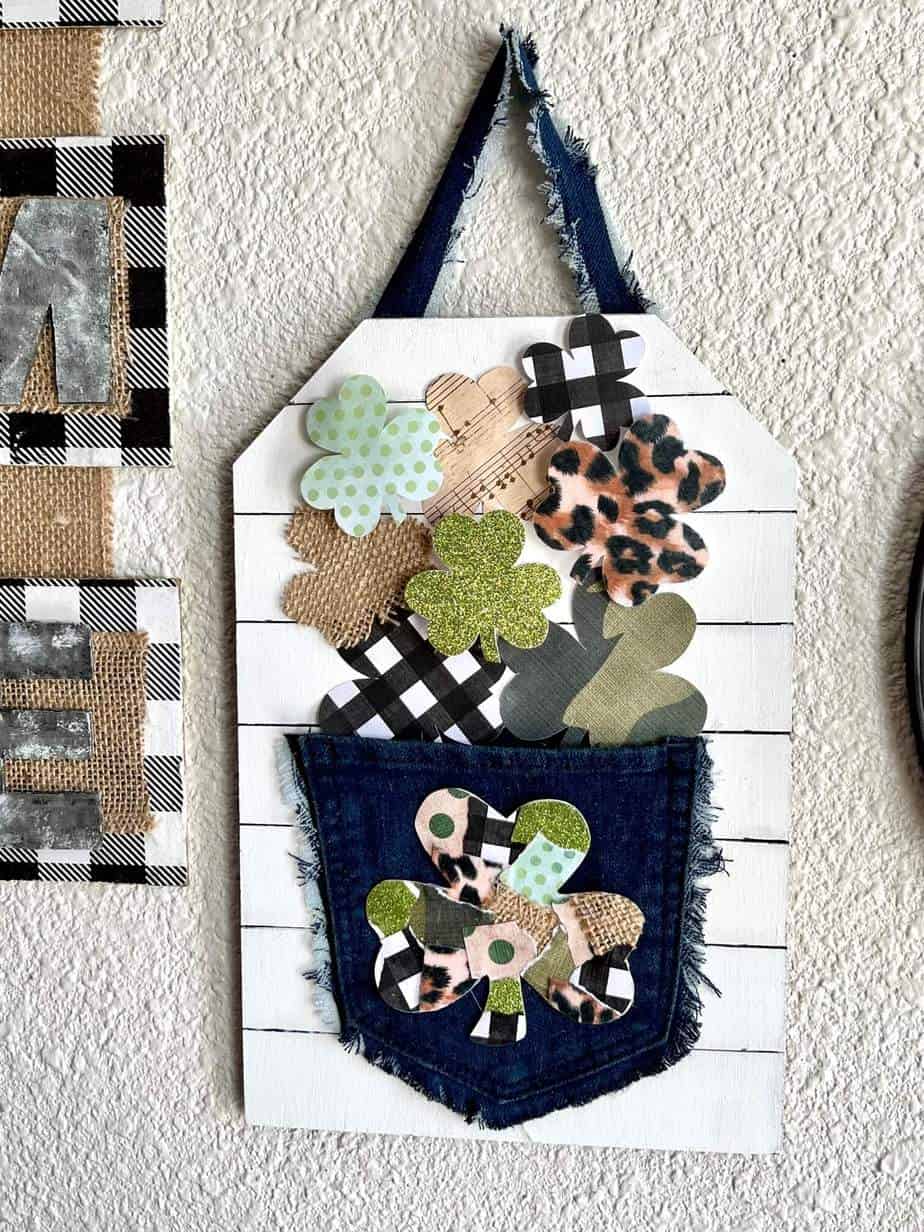 Wild Patchwork Shamrocks spilling out of a jeans pocket that are green glitter, leopard print, buffalo check, music sheet, and burlap with a faux shiplap background for DIY St. Patrick's Day and St. Patty's crafts and decor.