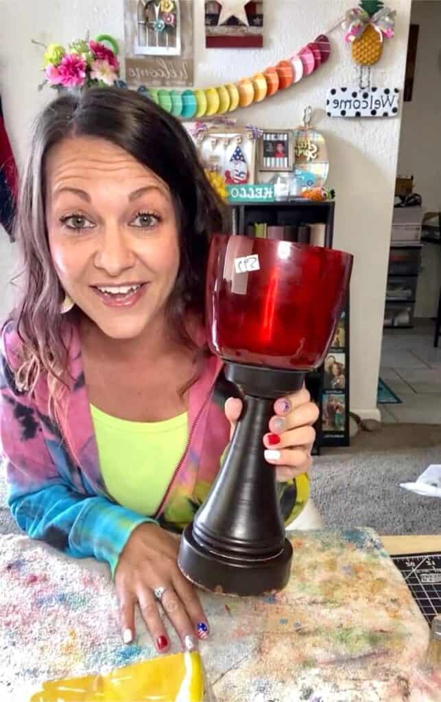 Amanda holding the thrift store candlestick before starting to paint it so the top is red and the bottom is black.