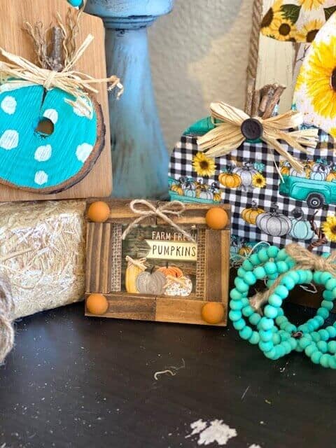 Mini jenga block frame with a dollar tree farm fresh pumpkins print inside next to a teal wood bead pumpkin.