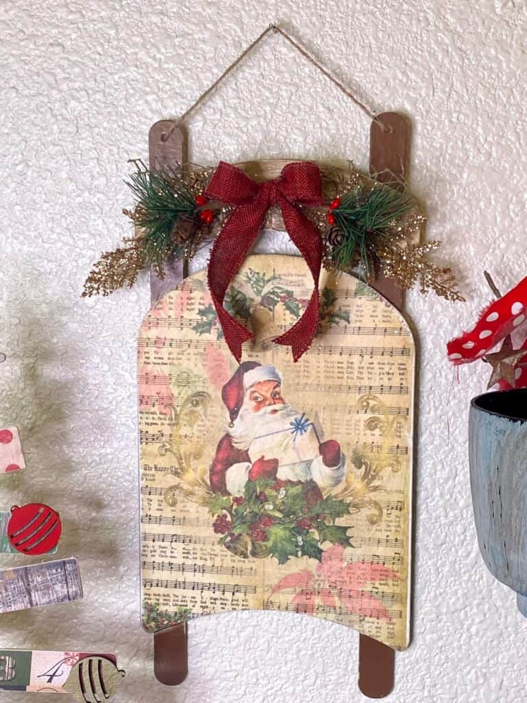 Dollar Tree Vintage Santa Sleigh with craft printable decoupaged onto wood and old music sheet background DIY Christmas Decor